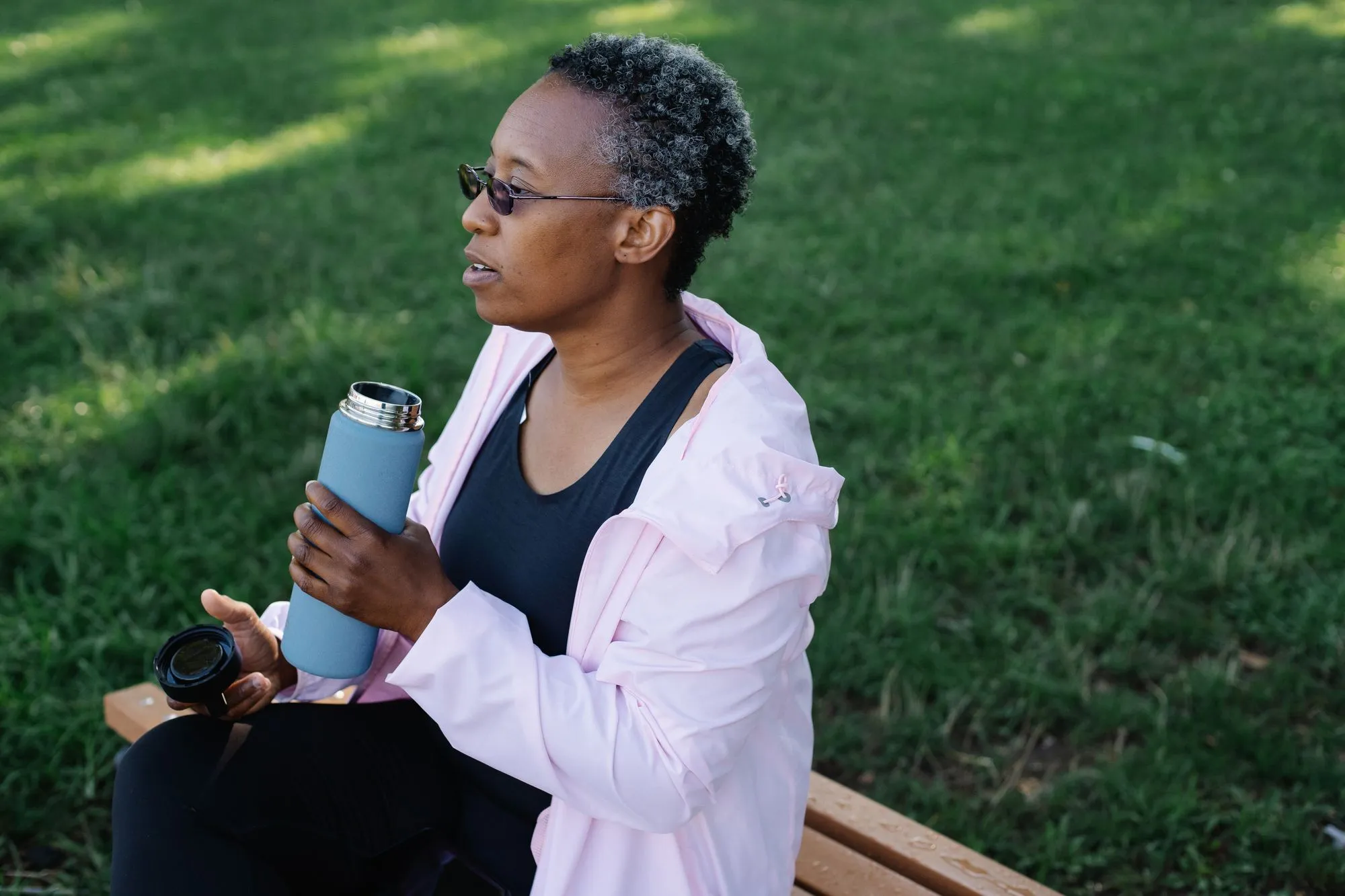 An older Black woman enjoying a drink and a peaceful moment on a park bench